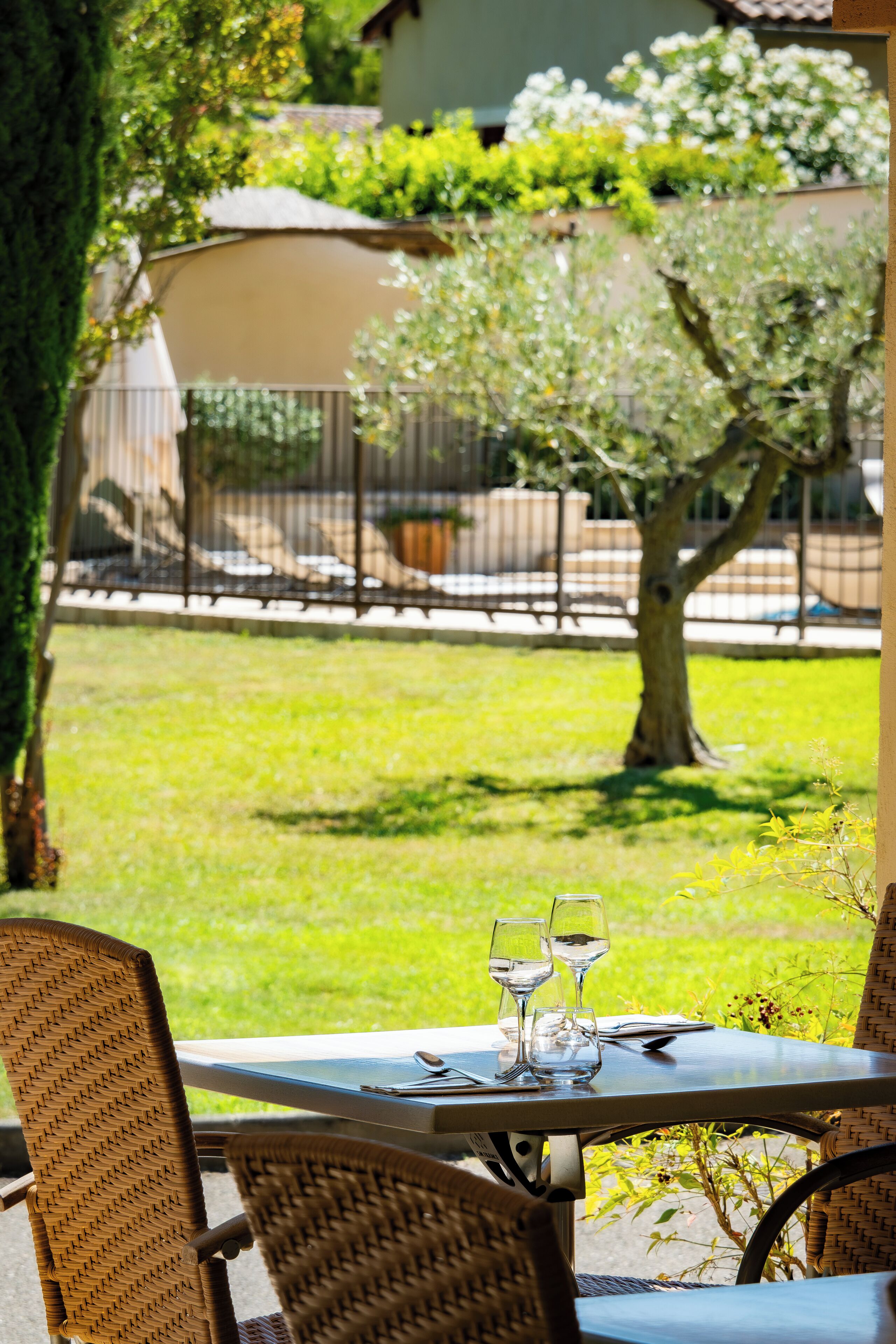 Un espace extérieur aménagé pour les repas, avec des chaises en osier et une table pour deux, offrant une vue sur une pelouse bien entretenue et un arbre.