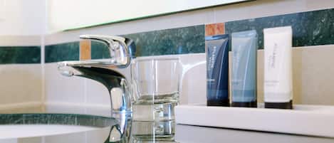Un baño moderno con un grifo cromado, un vaso de agua y artículos de aseo en un estante.