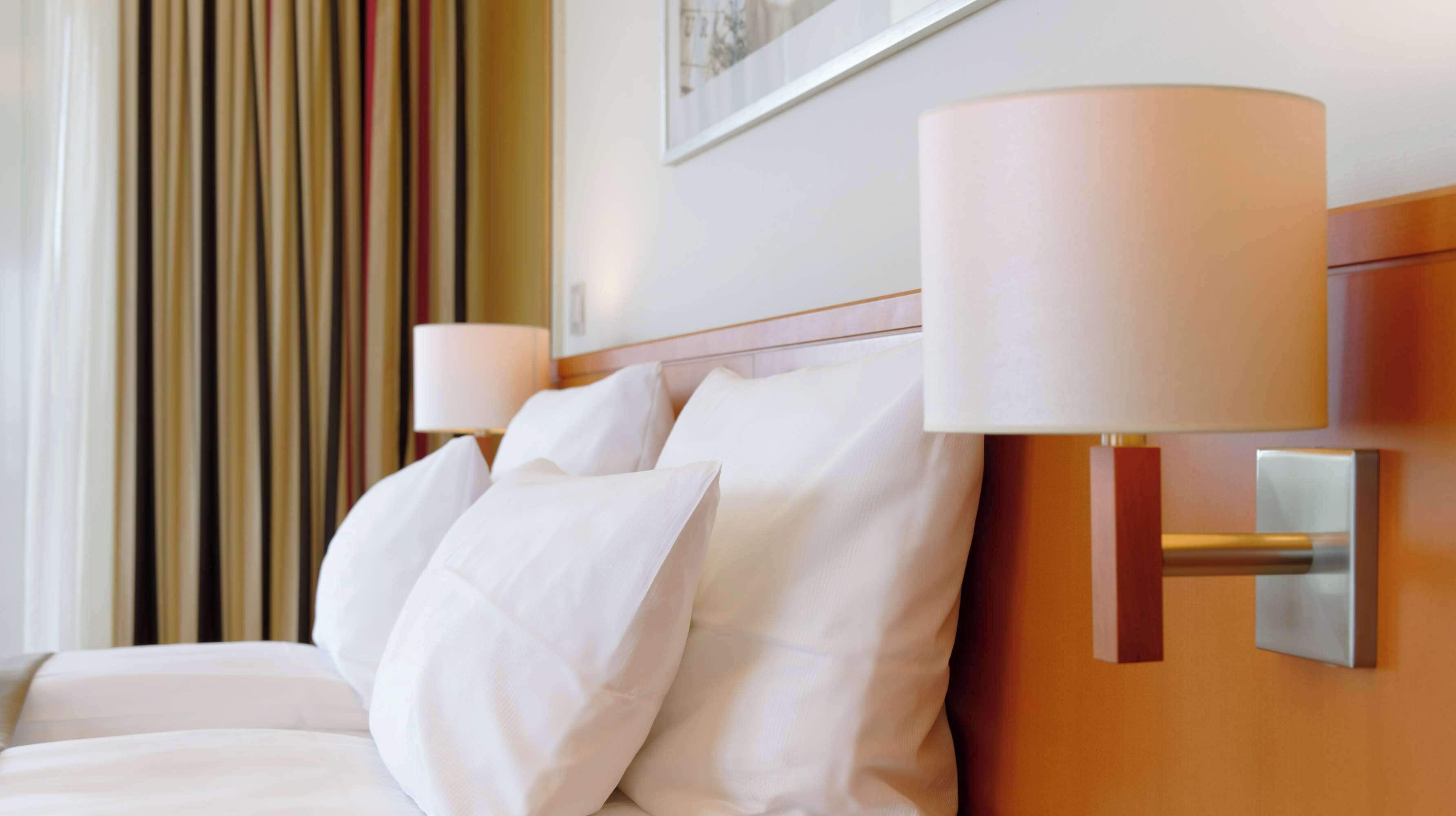 A hotel room with a neatly made bed, two bedside lamps, and a framed picture on the wall.