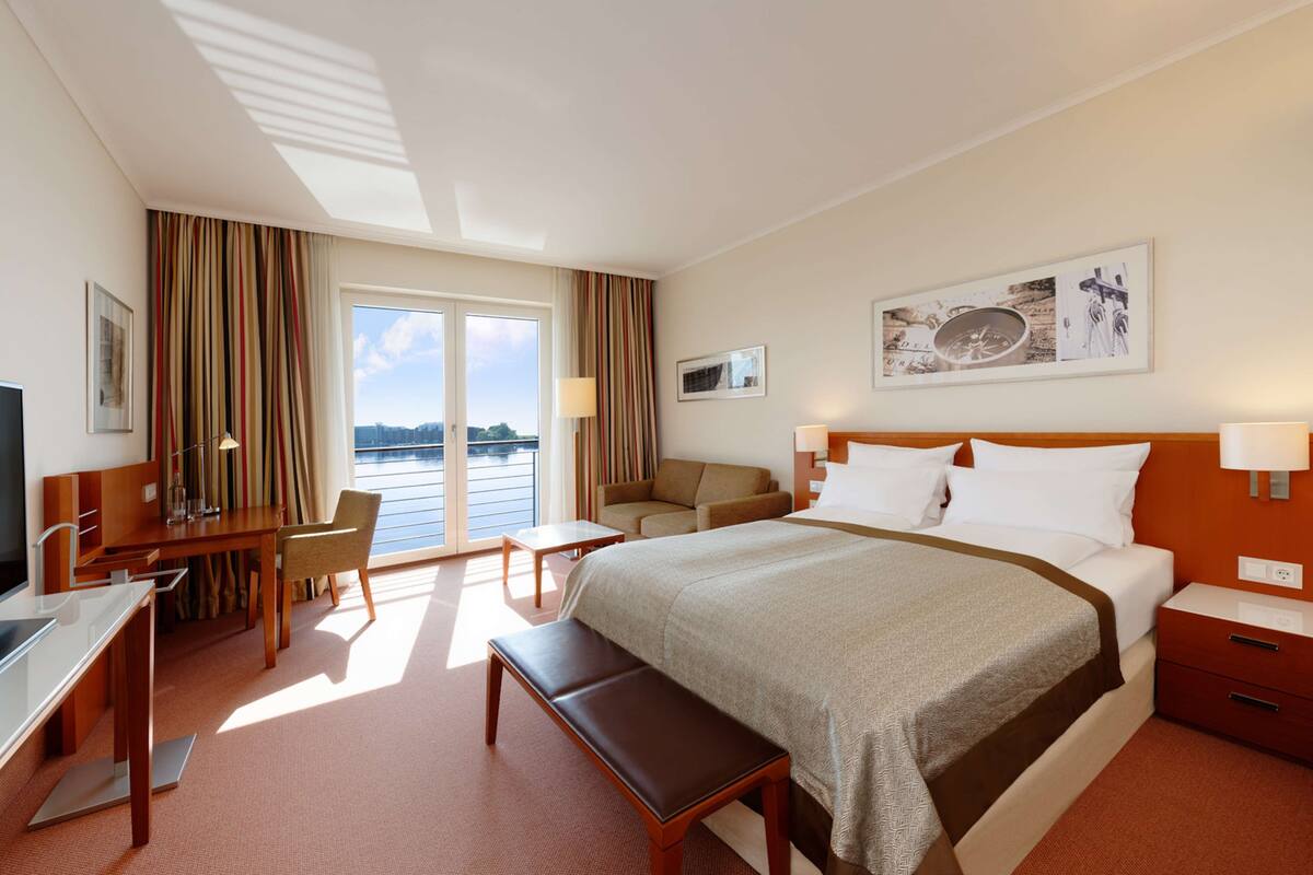 A hotel room with a bed, desk, chair, and a view of the outdoors.