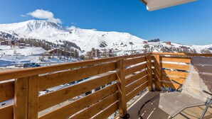 A wooden balcony with a view of a snow-covered mountain and a clear blue sky.