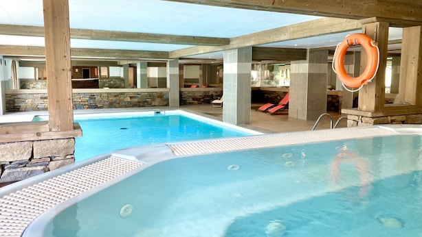 A large indoor swimming pool with a wooden deck area and lounge chairs.