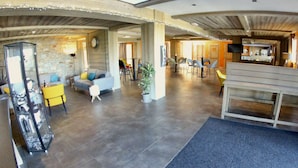 A spacious lobby with a stone wall, a seating area with a sofa and chairs, a reception desk, and a bar area with stools.