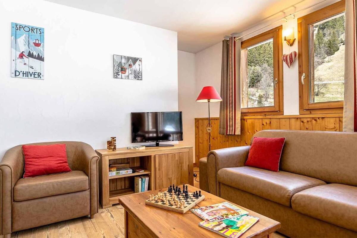 Un salon chaleureux avec un meuble TV en bois, un jeu d’échecs et deux canapés ornés de coussins rouges.