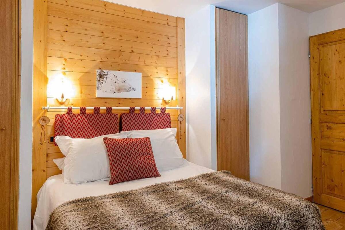 Une chambre à coucher avec une tête de lit en bois, un lit avec des oreillers blancs et rouges, un tapis moelleux et une porte en bois.