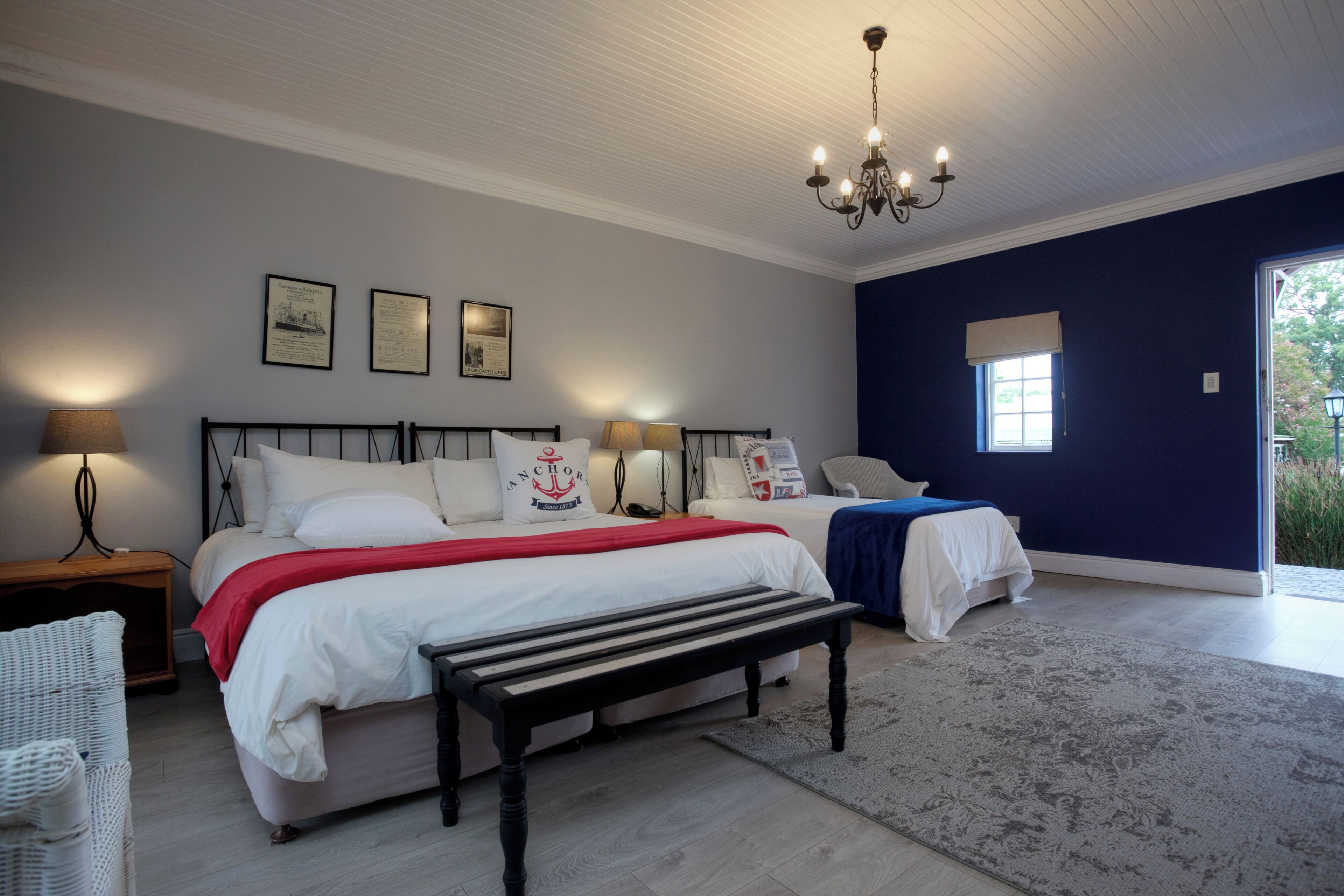 A bedroom with a large bed, a smaller bed, a bench, a nightstand, a lamp, and a chandelier.