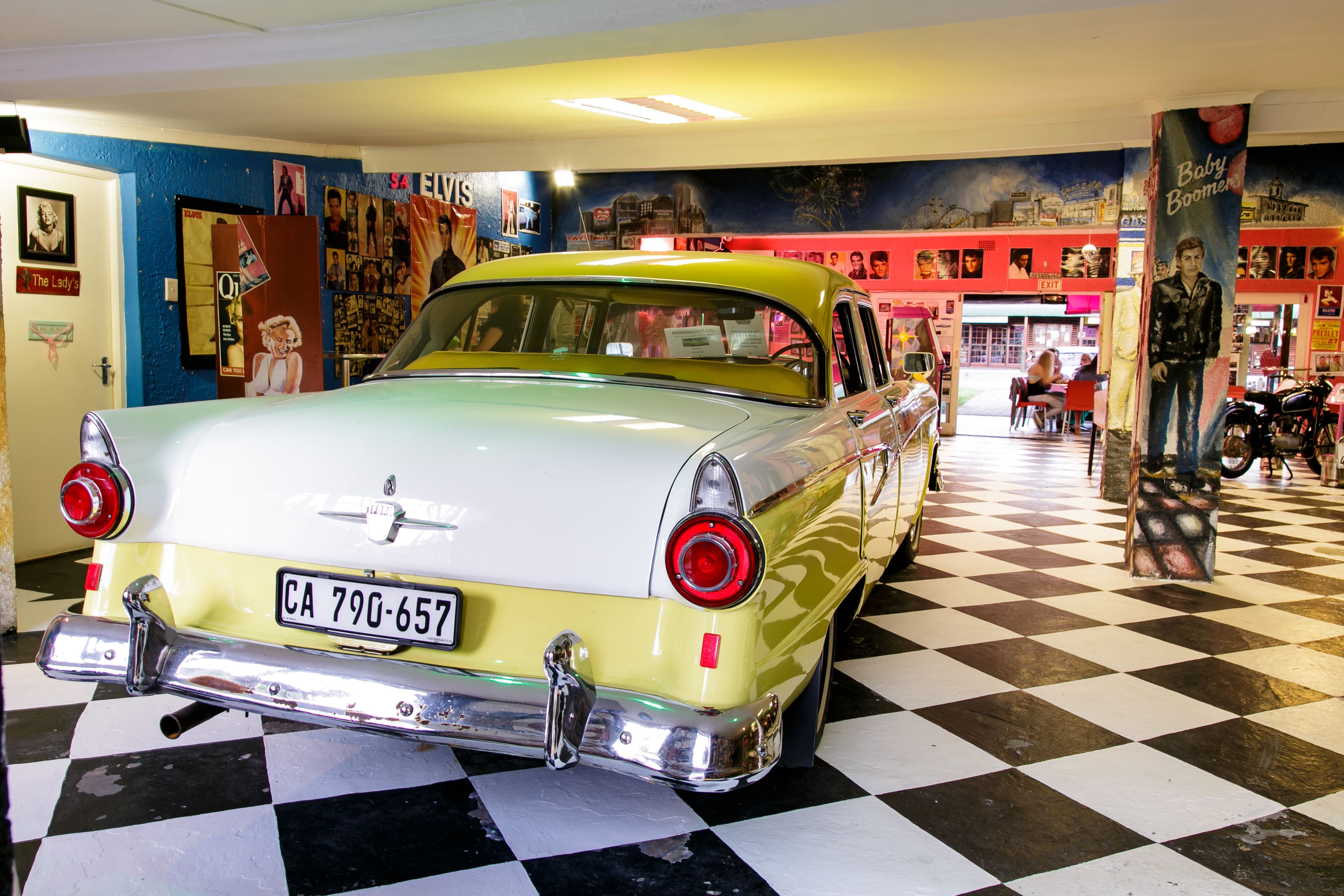 A vintage car in a showroom with a checkered floor and colorful murals on the walls.