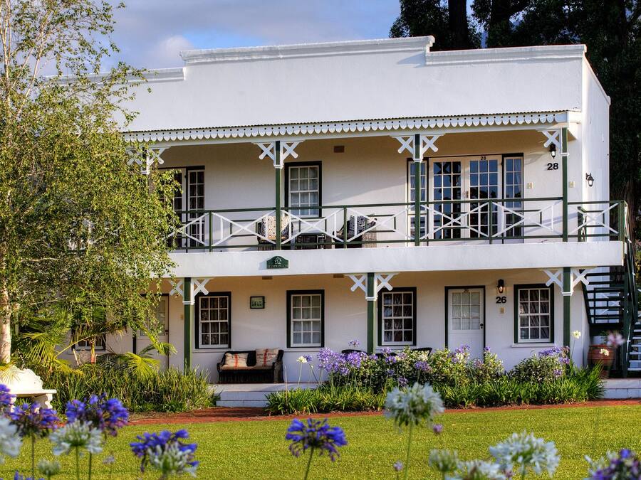 Ein weißes, zweistöckiges Gebäude mit Balkon, Hausnummer 28, und ein Garten mit violetten Blumen.
