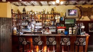 Un bar con estantes de madera llenos de botellas, un televisor montado en la pared y una cabeza de animal decorativa en la pared.