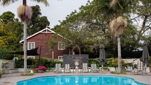 A swimming pool with lounge chairs and umbrellas, surrounded by trees and a house.