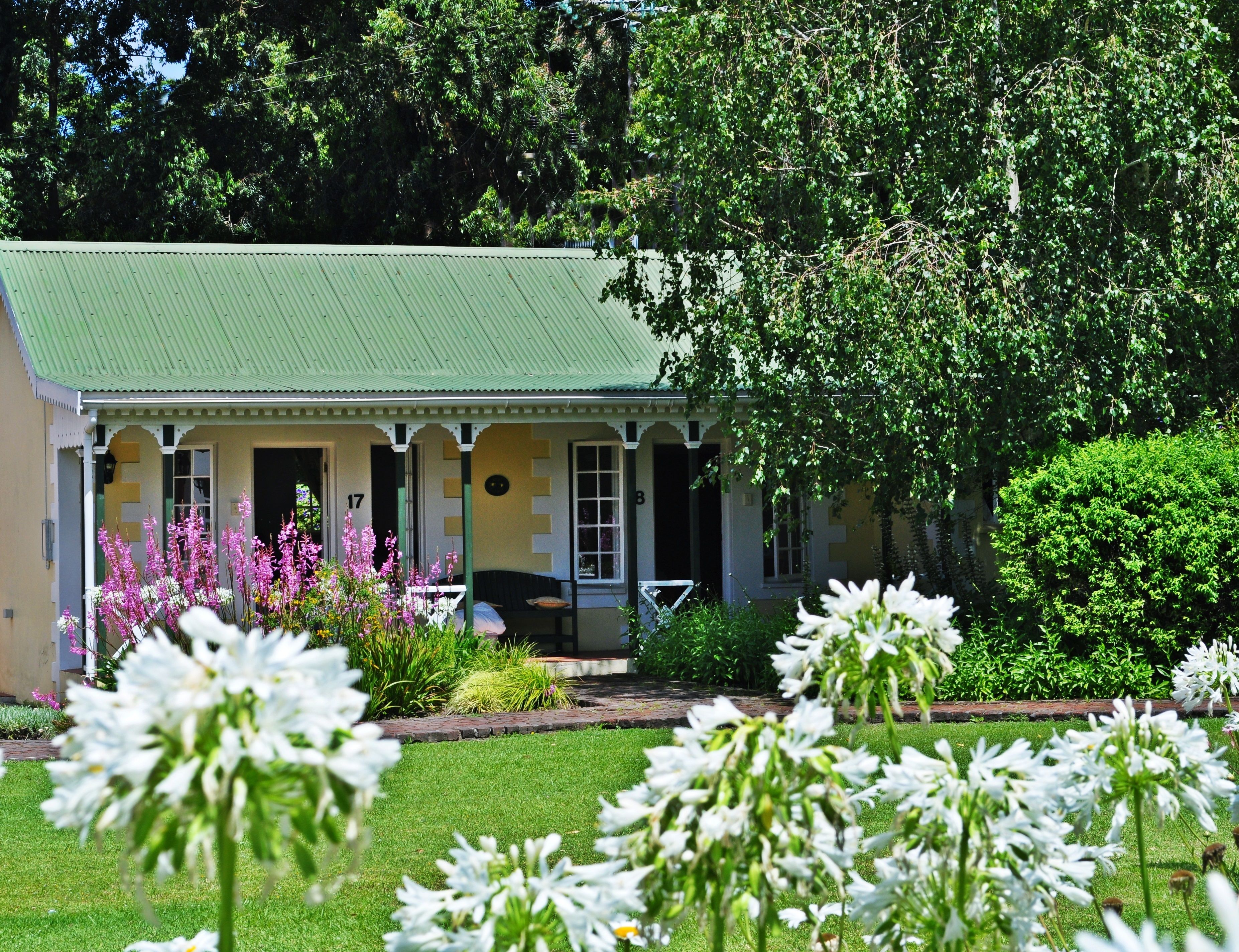 Una casa con techo verde, un porche con barandillas blancas y un jardín con flores blancas.