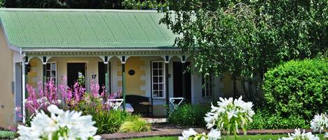 Una casa con techo verde, un porche con barandillas blancas y un jardín con flores blancas.