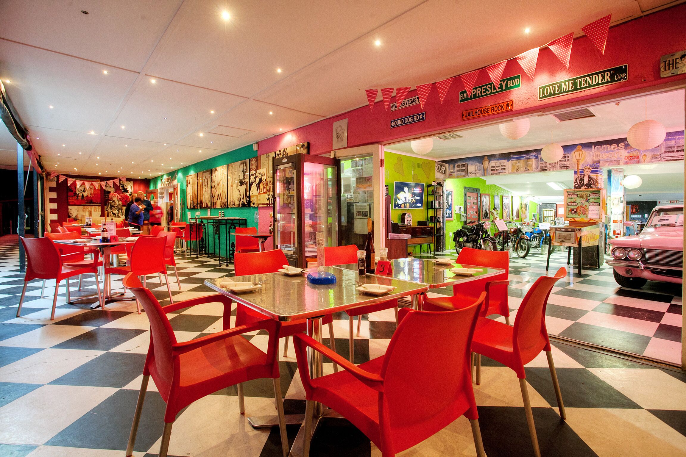 A diner with red chairs and tables, a checkered floor, and a neon sign.
