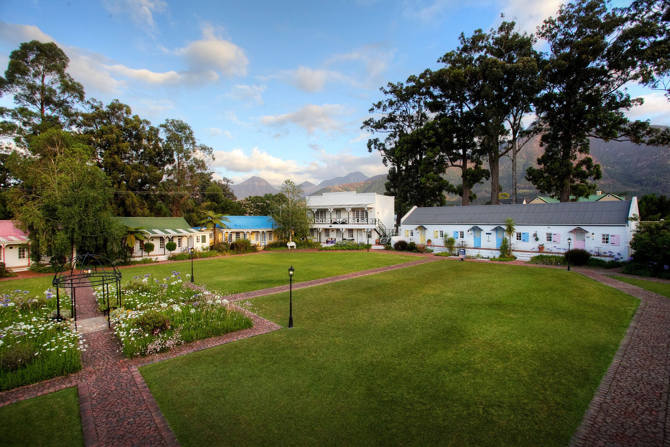 Un hotel con un amplio jardín, un pabellón y montañas al fondo.