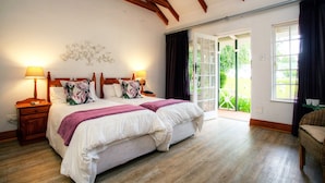 Une chambre avec deux lits, un plancher en bois, une grande fenêtre avec des rideaux et une vue sur la verdure.