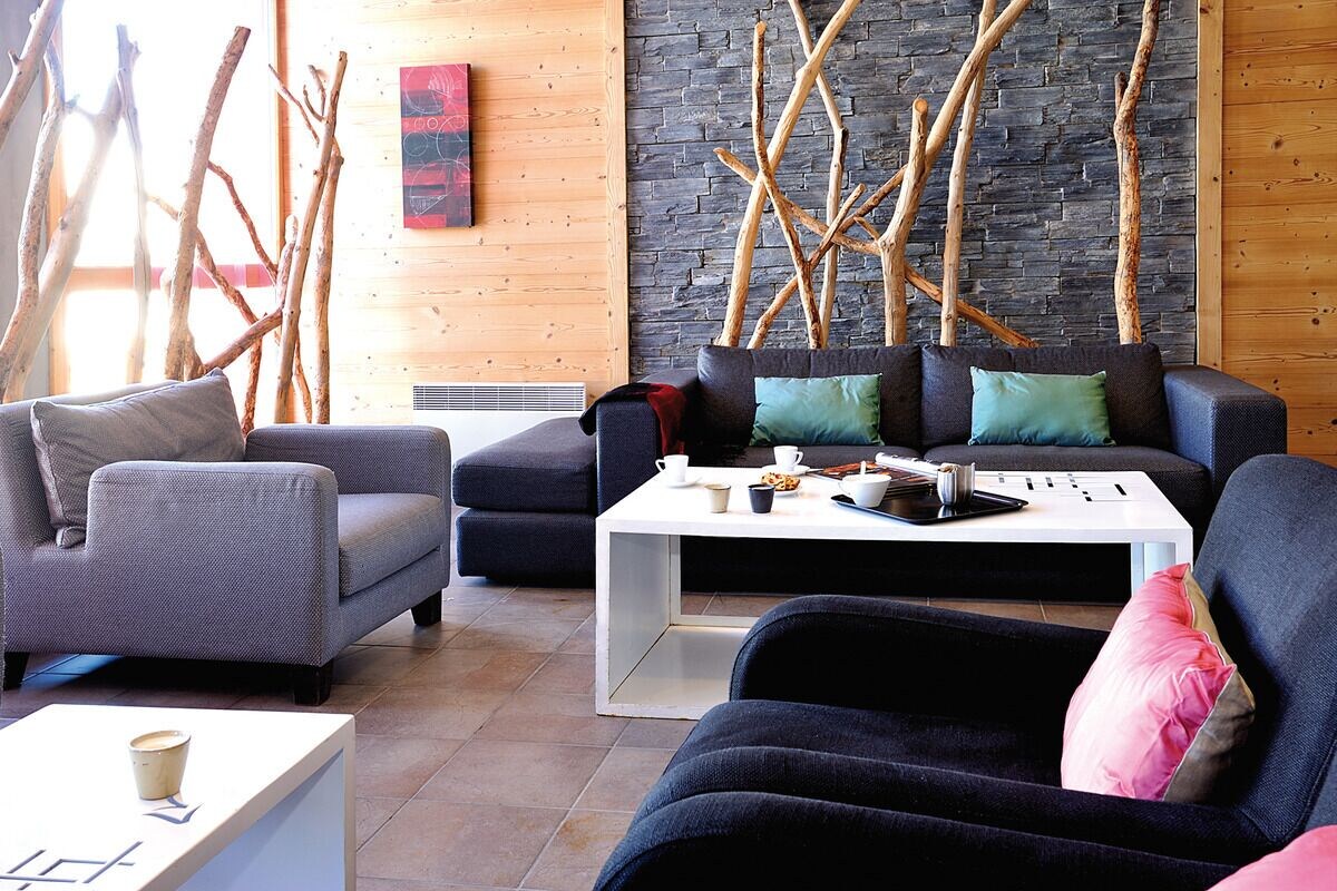 A modern living room with a sofa, armchairs, a coffee table, and decorative branches against a stone wall.