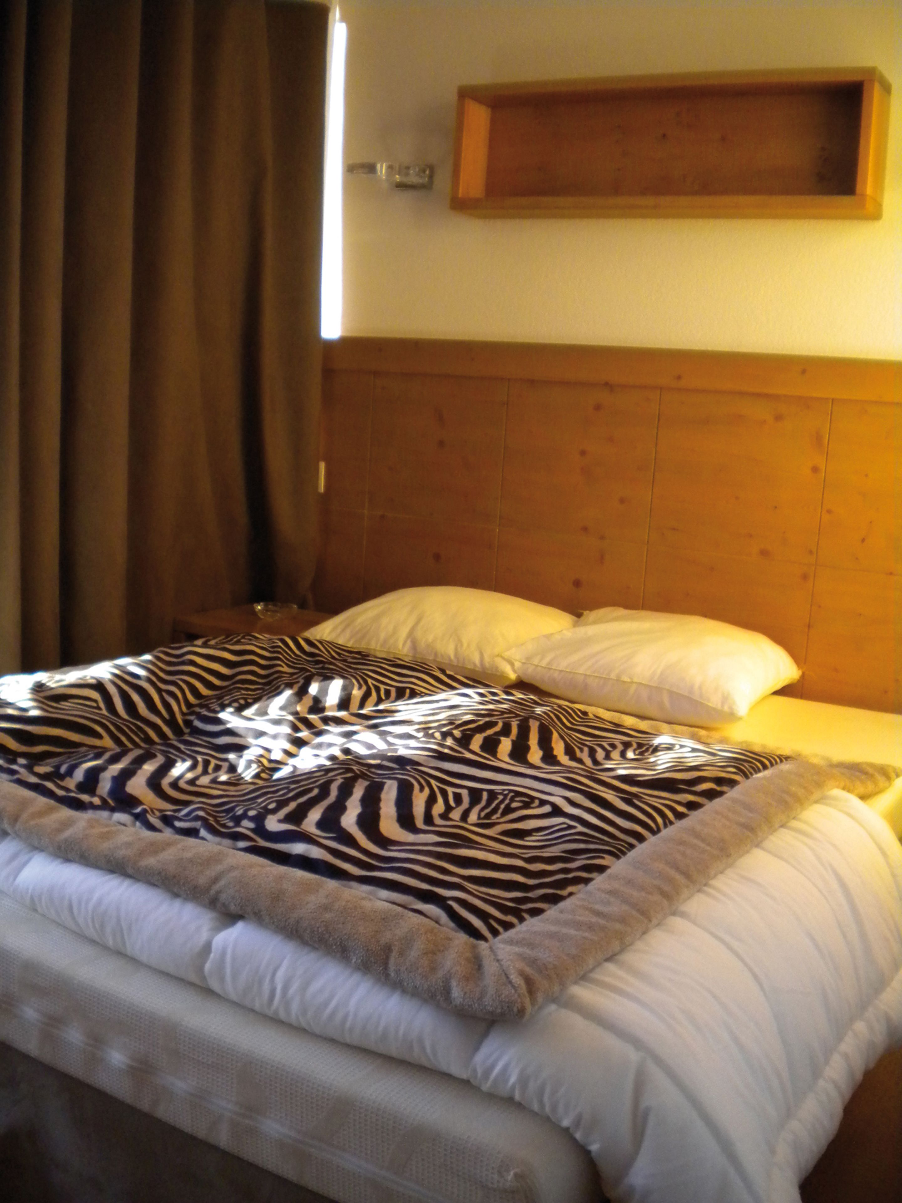A bed with a zebra-patterned blanket, a wooden headboard, and a bedside shelf.
