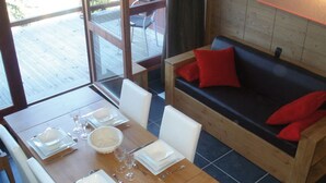 Un comedor con una mesa de madera dispuesta para cuatro personas, un sofá con cojines rojos y vistas al exterior a través de grandes ventanales.