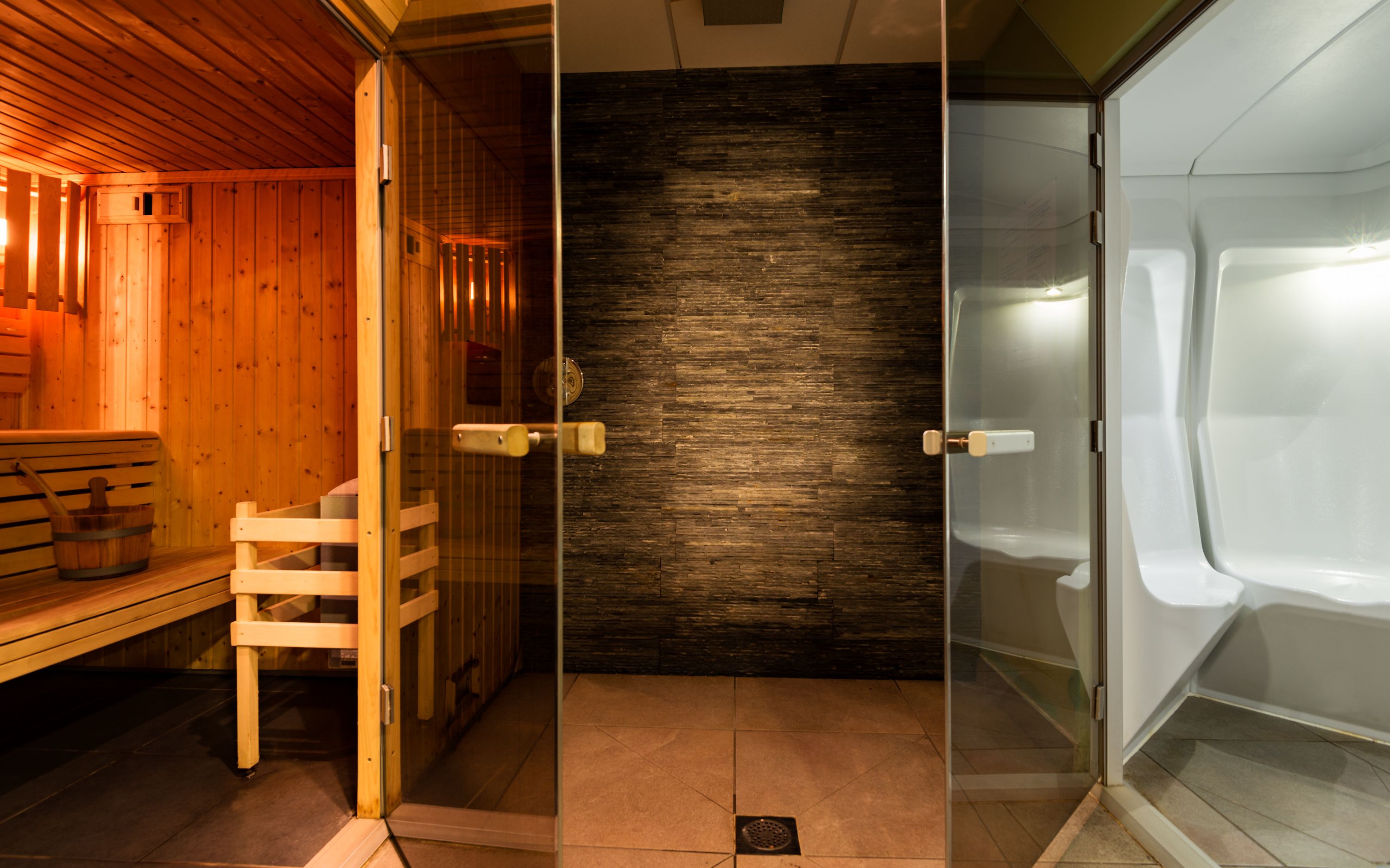 Una sala de sauna con bancos de madera, una puerta de cristal y suelo de baldosas.
