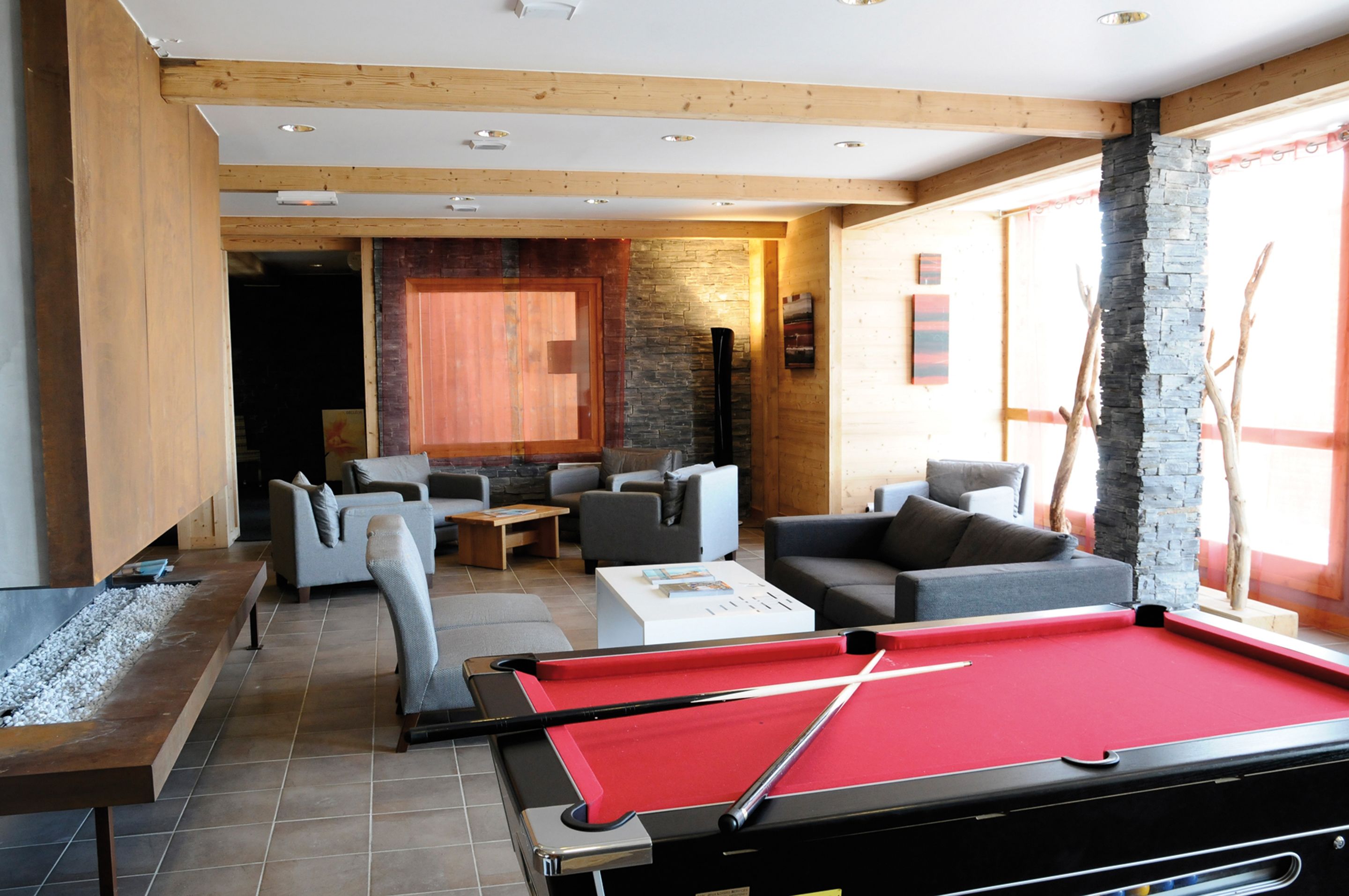 Une table de billard dans une pièce dotée d’une cheminée, de canapés et d’un mur décoratif en pierre.