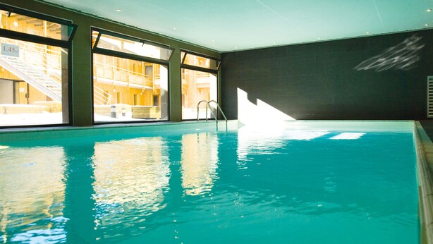 An indoor swimming pool with clear water, large windows, and a visible staircase leading outside. - Résidence Lagrange Vacances Le Pic de l'Ours (Font-Romeu-Odeillo-Via)