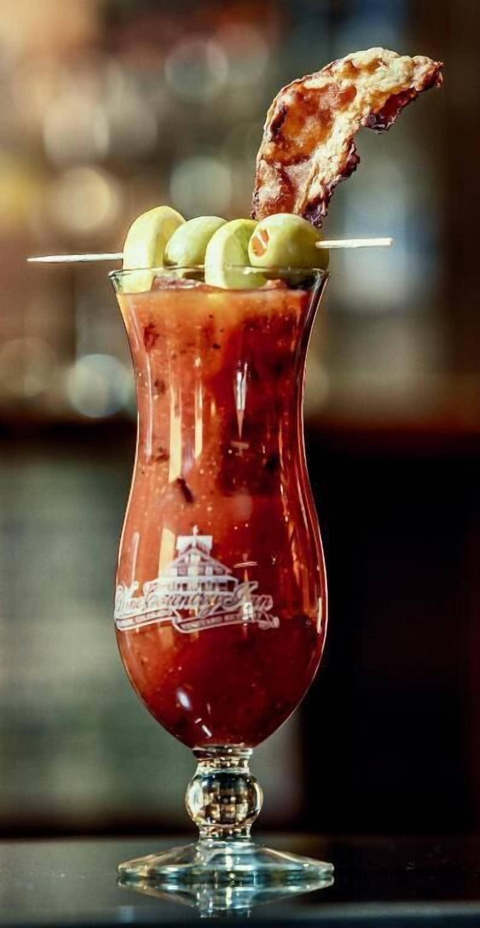 Un cóctel en una copa con aceitunas y una tira de tocino como decoración.