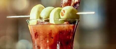 Un cóctel en una copa con aceitunas y una tira de tocino como decoración.