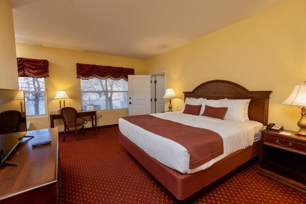 A hotel room with a large bed, a desk, a chair, and a window with curtains.