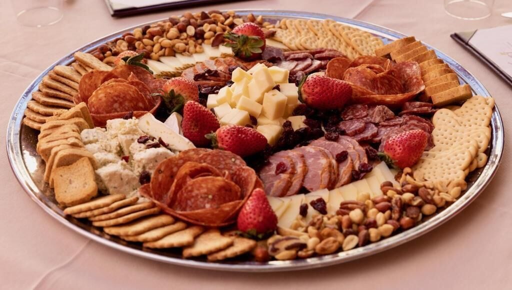 A platter with various cheeses, fruits, and nuts.