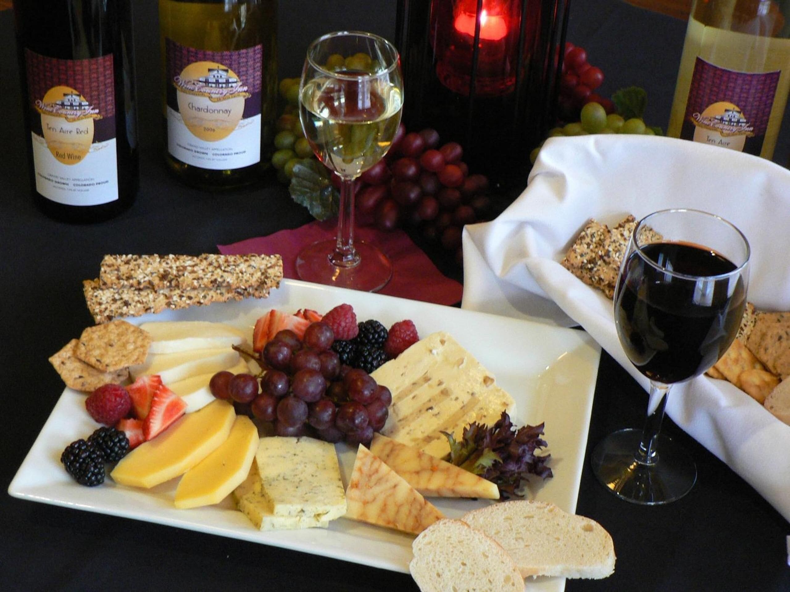 A charcuterie board with various cheeses, fruits, and crackers, accompanied by wine bottles and glasses.