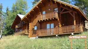 A wooden chalet with a balcony, surrounded by trees. - Madame Vacances Résidence La Crête du Berger (Le Dévoluy)
