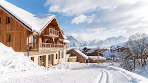 A wooden chalet with a balcony, surrounded by snow-covered mountains and a clear sky. - Résidence Lagrange Vacances Les Balcons des Aiguilles (Fontcouverte-la-Toussuire)