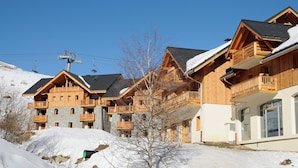 A ski resort with wooden buildings, balconies, and a ski lift in the background. - Résidence Lagrange Vacances Les Balcons des Aiguilles (Fontcouverte-la-Toussuire)