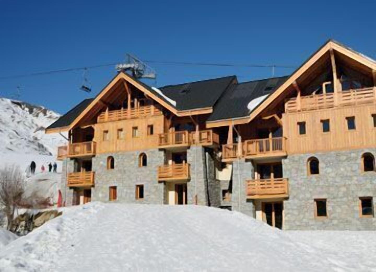 Un edificio de madera de varios pisos con balcones, con una nevada cadena montañosa al fondo.