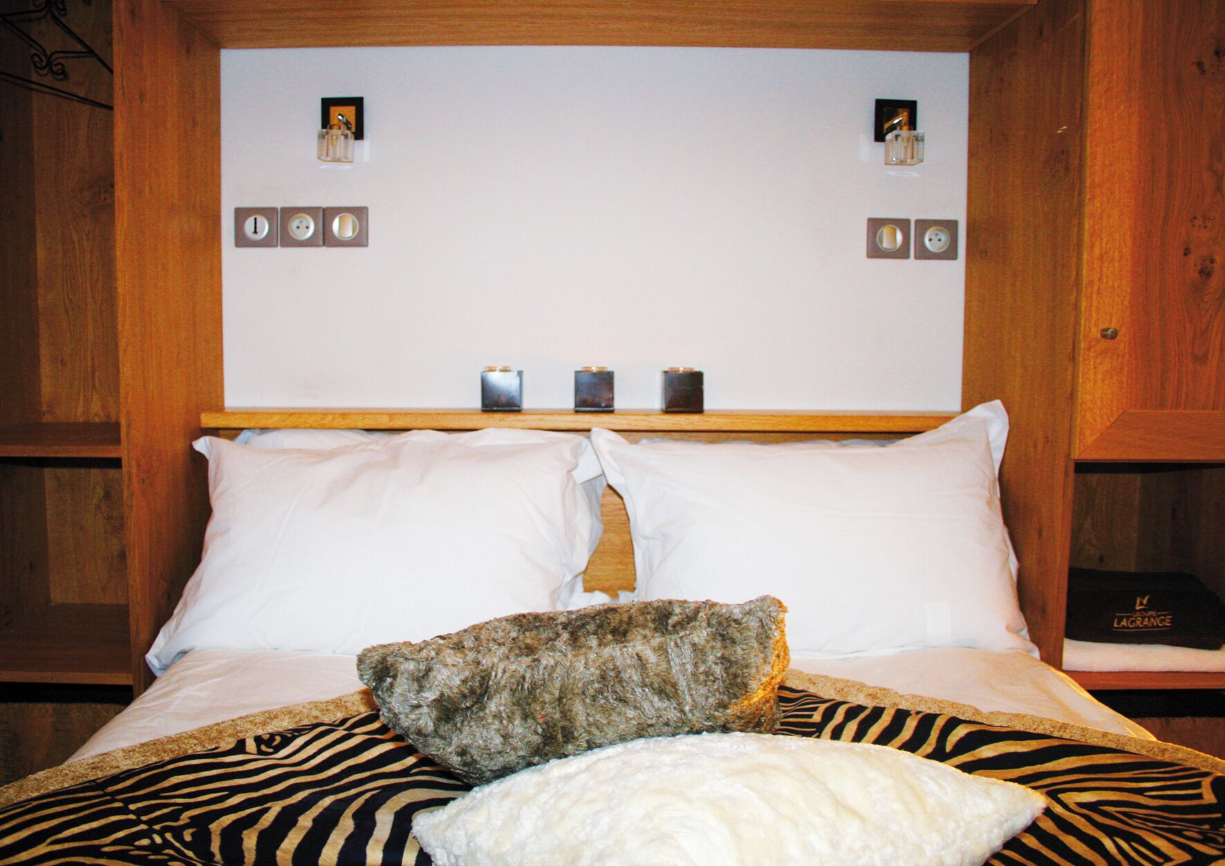 Un lit avec du linge de lit blanc, une couverture à motifs zébrés et un gros rocher. Il y a des horloges accrochées au mur au-dessus du lit.
