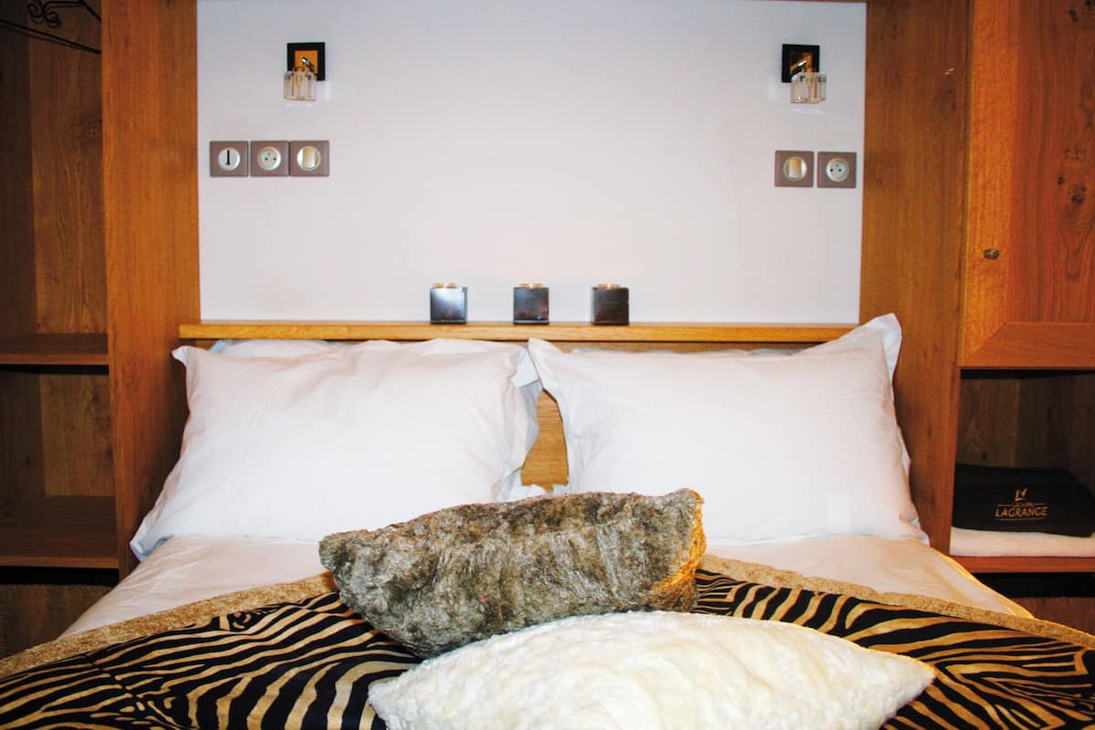 Un lit avec du linge de lit blanc, une couverture à motifs zébrés et un gros rocher. Il y a des horloges accrochées au mur au-dessus du lit.