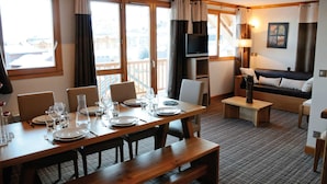 A dining area with a wooden table set for four, a sofa, and a TV in the corner. - Résidence Lagrange Vacances Les Balcons des Aiguilles (Fontcouverte-la-Toussuire)