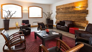 A modern lounge area with wooden furniture, a red patterned rug, and a wooden wall panel. - Résidence Lagrange Vacances Les Balcons des Aiguilles (Fontcouverte-la-Toussuire)