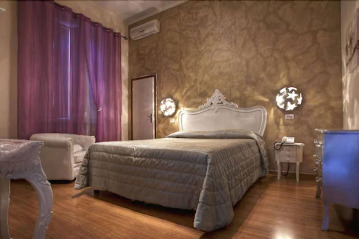 Ein Schlafzimmer mit einem Bett, einem Nachttisch, einem Sessel, einer Kommode und einer Klimaanlage.