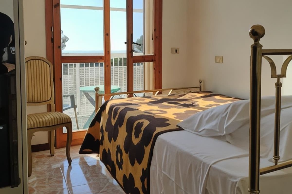 Un dormitorio con cama, una silla, ventana y balcón.