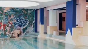 A modern indoor pool area with a large mural on the wall, a clear pool, and a reception desk. - Hotel Atlantico (Rosignano Marittimo)