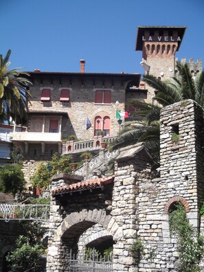 Un edificio de piedra histórico con una torre que dice "LA VELA", con ventanas arqueadas, un balcón y una escalera de piedra.