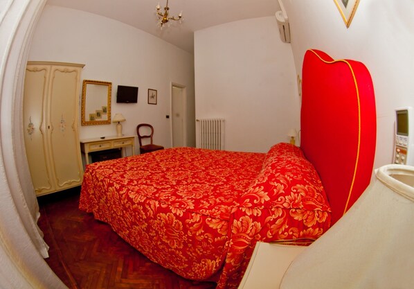Een slaapkamer met een rood bloemenbedekt, een witte kast, een spiegel, een bureau en een rode hoofdbord.