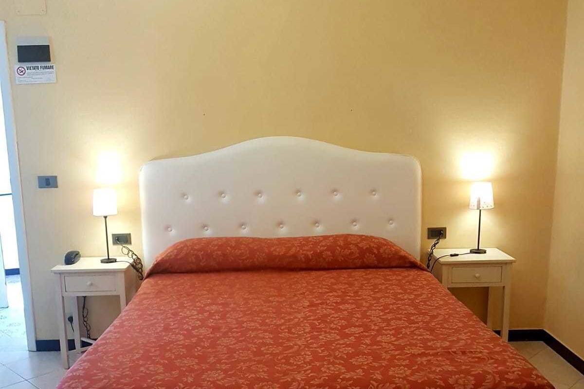 A hotel room with a large bed, two bedside tables with lamps, a chandelier, and a sign on the wall.