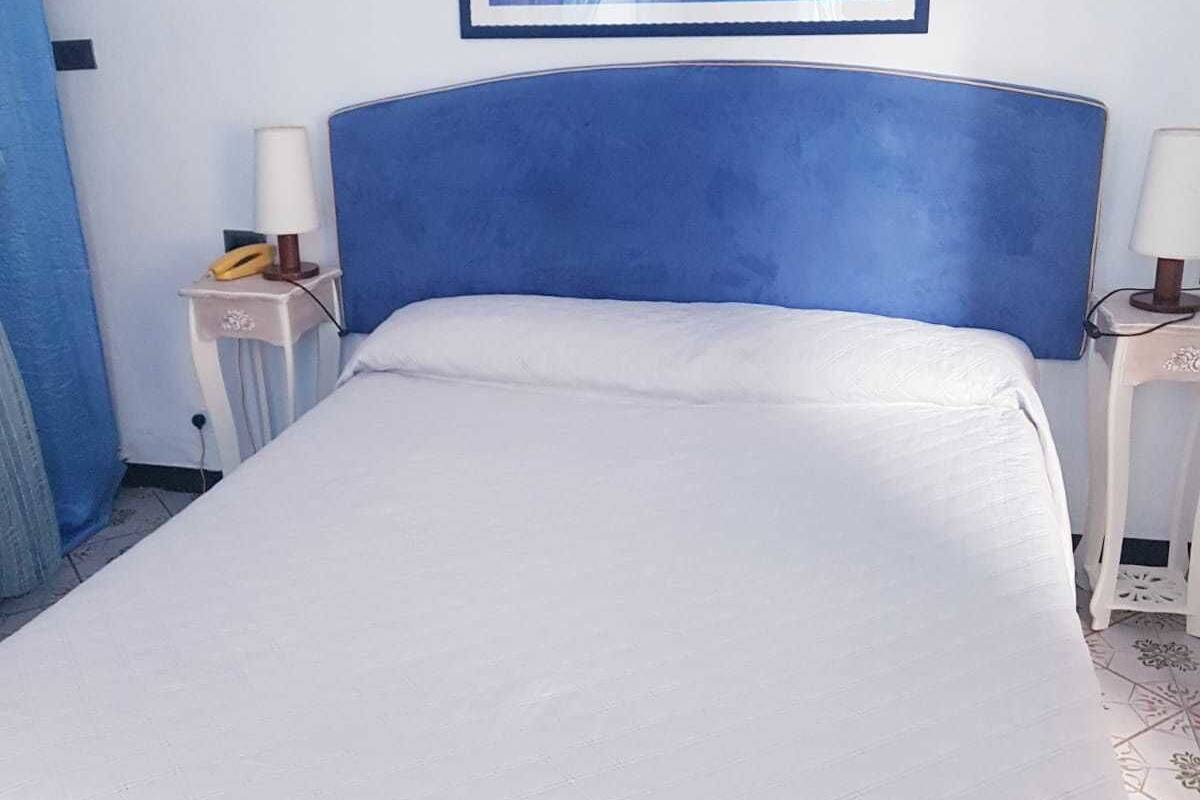 A hotel room with a bed, two bedside tables, a framed picture on the wall, and a blue headboard.