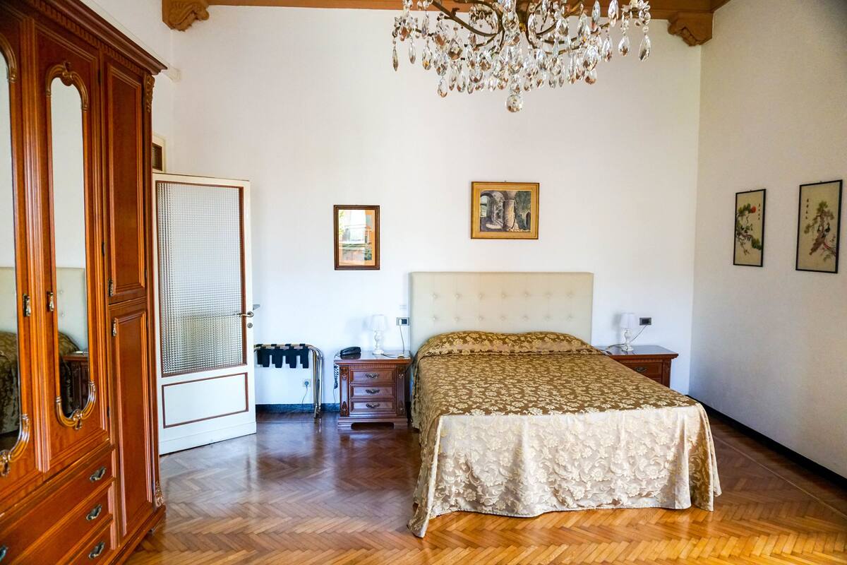 A bedroom with a large bed, wooden wardrobe, and a chandelier.