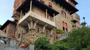 Um edifício de pedra histórico com um portão vermelho, uma varanda com esculturas detalhadas e uma placa com a inscrição 
