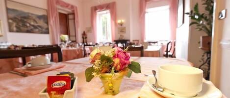 Un coin repas avec une table dressée pour deux personnes, agrémenté d’un vase de fleurs, d’une tasse et d’une boîte de chocolats Eridania Tropica.