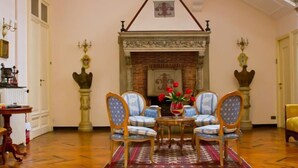Um quarto com lareira, duas poltronas, uma mesa pequena com um vaso de flores e um tapete estampado.