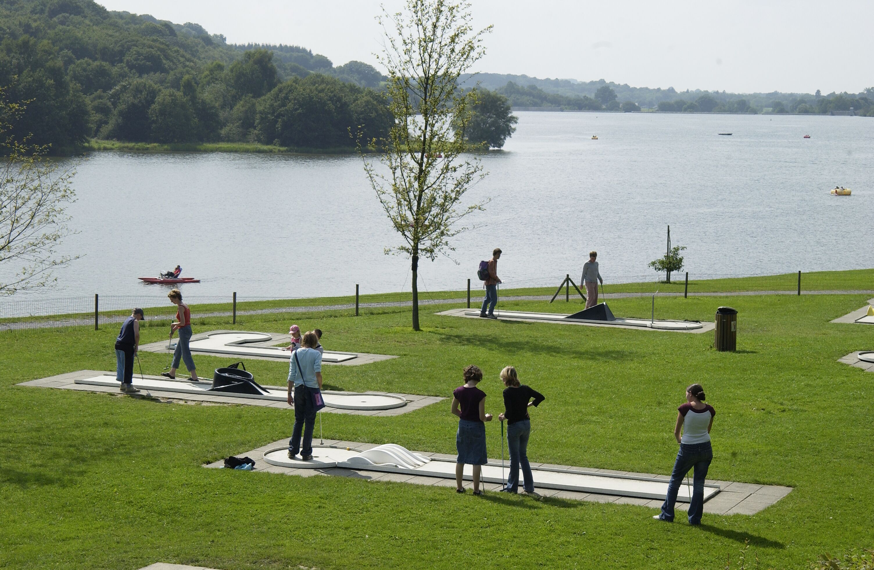 A park with a lake, people engaging in activities, and a boat in the water.